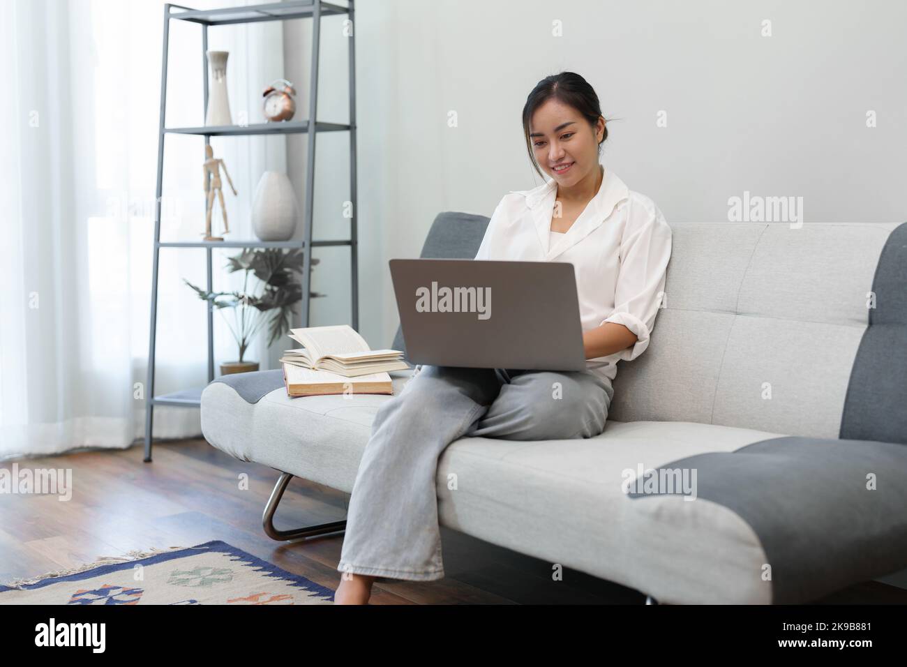Portrait of a young Asian woman sitting on the sofa using a computer ...
