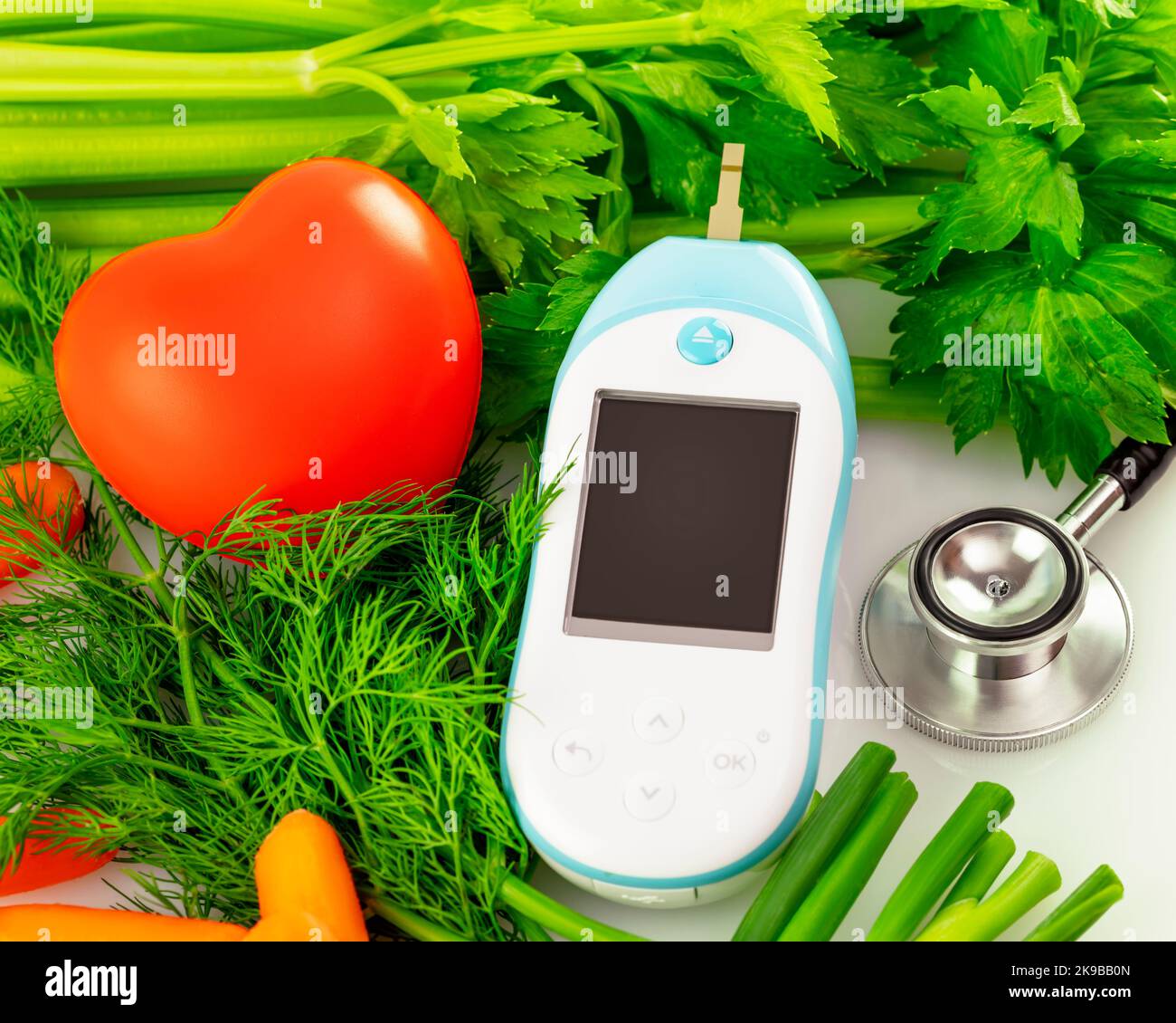 Health care and dieting concept with fresh vegetables and stethoscope, glucose meter and red heart on a white table. Control of health with diet Stock Photo