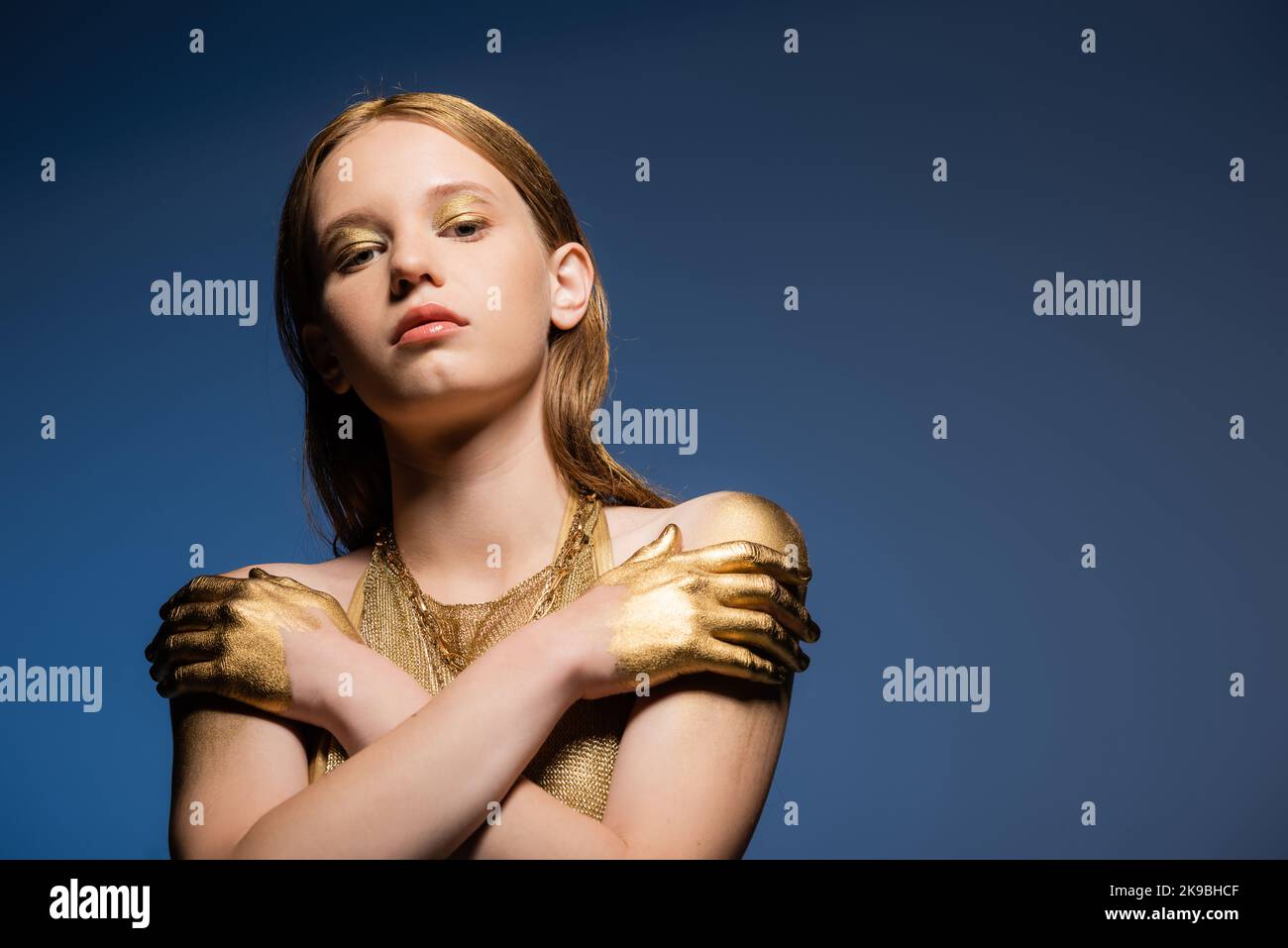 Pretty model with makeup and golden paint on hands looking at camera isolated on blue Stock Photo