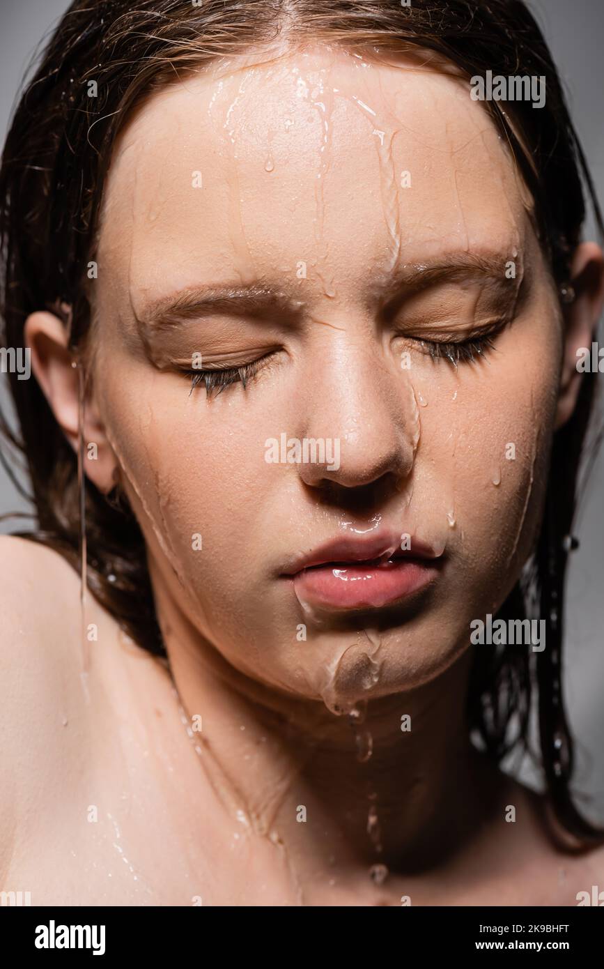 Close up view of water pouring down on face of young model isolated on grey Stock Photo