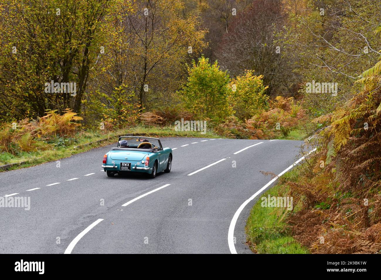 An MG Midget (1973) sports car being driven with the top down during autumn on a country road in Scotland, UK Stock Photo