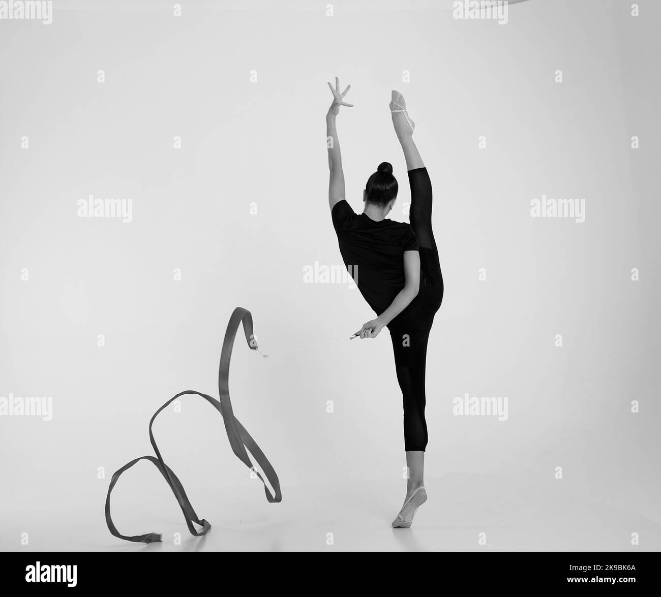 a girl from rhythmic gymnastics in a standing bodysuit shows an exercise with a ribbon in vertical splits Stock Photo