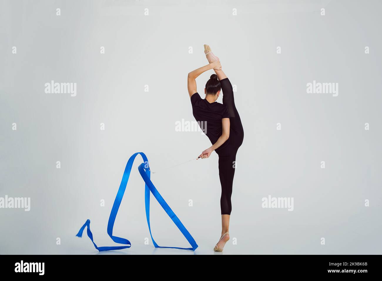 a girl from rhythmic gymnastics in a standing bodysuit shows an exercise with a ribbon in vertical splits Stock Photo