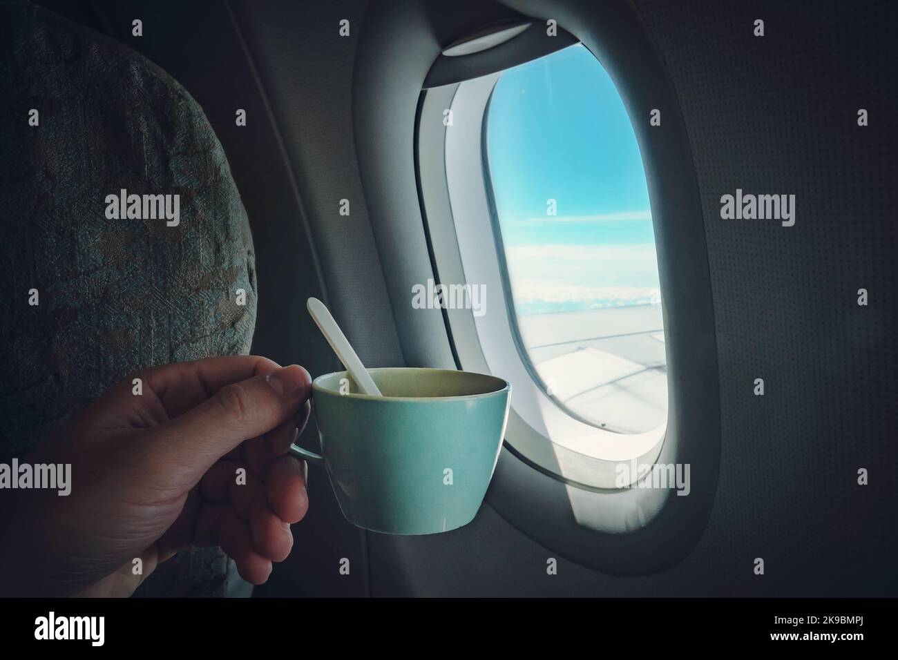 A man's hand holding a Cup of coffee in front of window of plane in