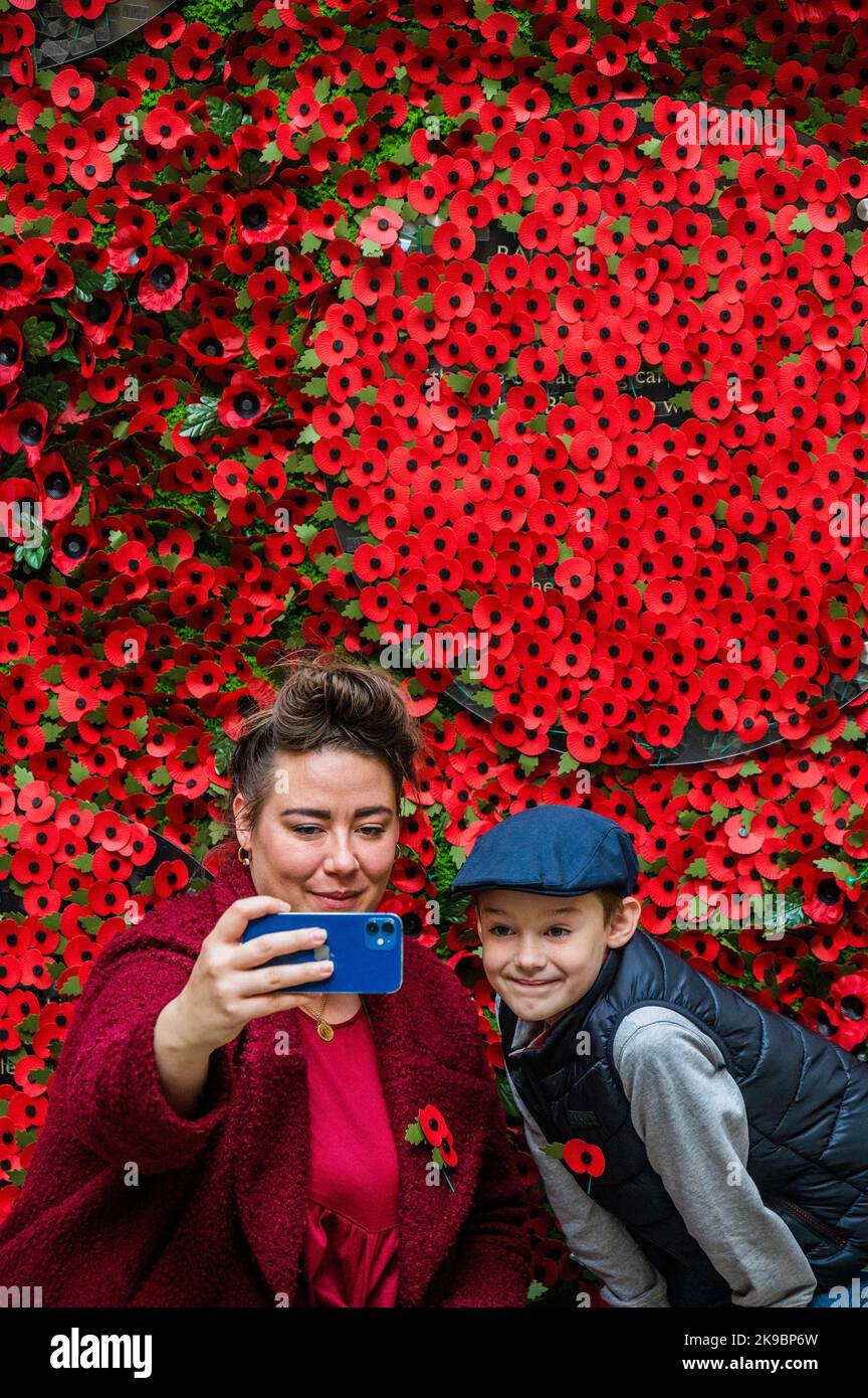 London, UK. 27 Oct 2022. A mother and son take. aselfie having bought their poppies - The Royal British Legion's Poppy Appeal 2022 launches with a 6-metre-wide wall of poppies featuring stories of veterans, RBL beneficiaries (many having received lifechanging support) and their families - the people behind the poppy. Members of the public were invited to take a paper poppy from the wall to uncover the stories. The charity is urging people to wear a poppy this year to show that they care and that the service and sacrifice of serving personnel, veterans and their families will never be forgotten Stock Photo