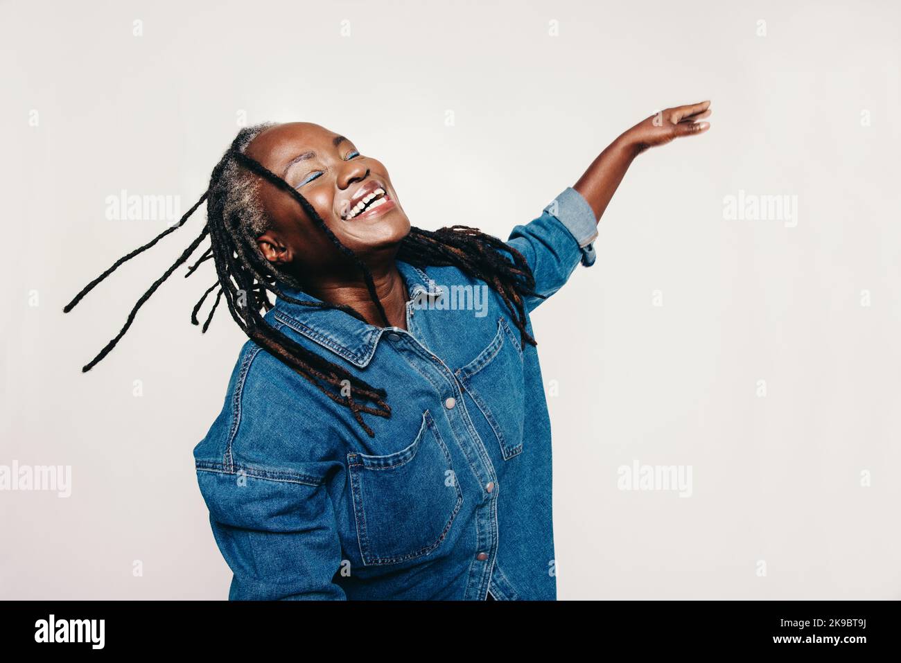 Happiness in the studio. Mature woman with dreadlocks laughing with her eyes closed and her arms outstretched. Joyful middle-aged woman wearing a deni Stock Photo