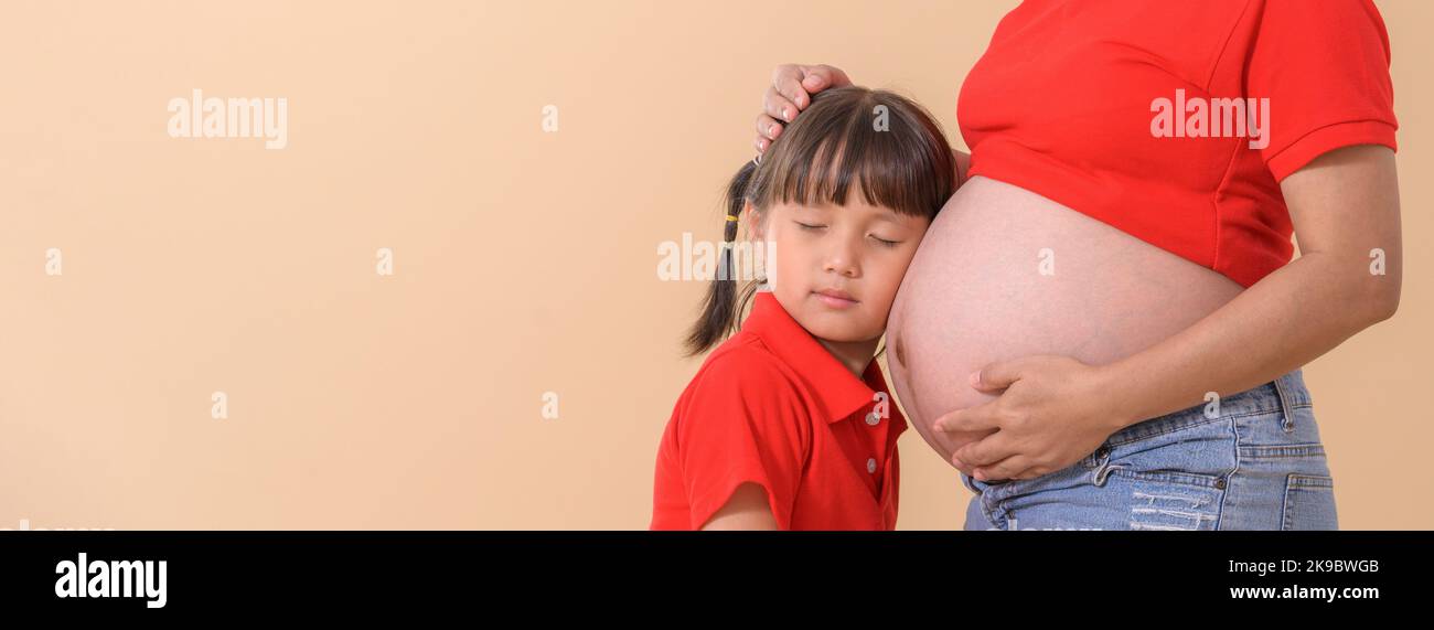 Girl listening baby's heartbeat hugging pregnant mother's belly Stock Photo