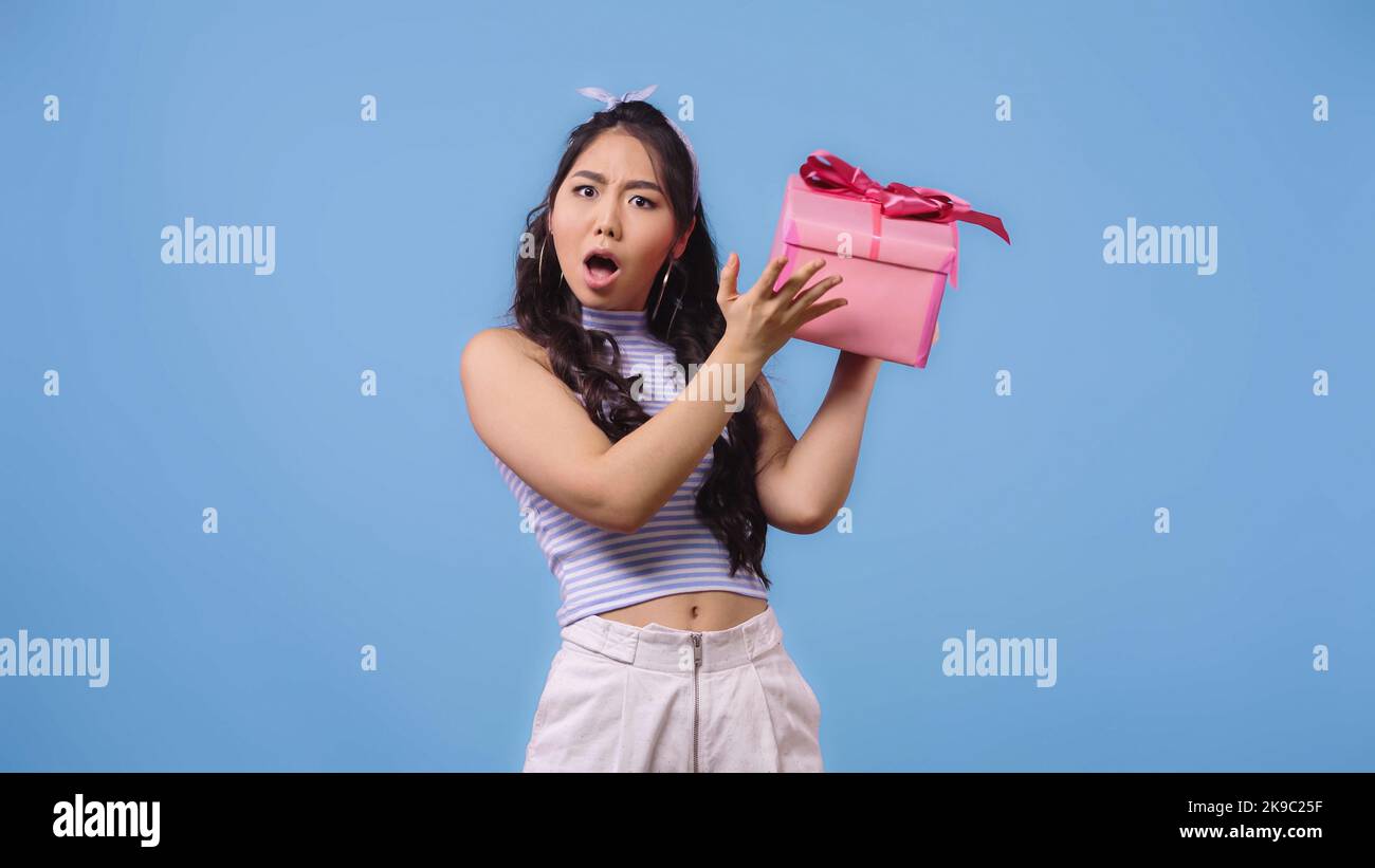 shocked asian woman shaking wrapped gift box isolated on blue Stock ...