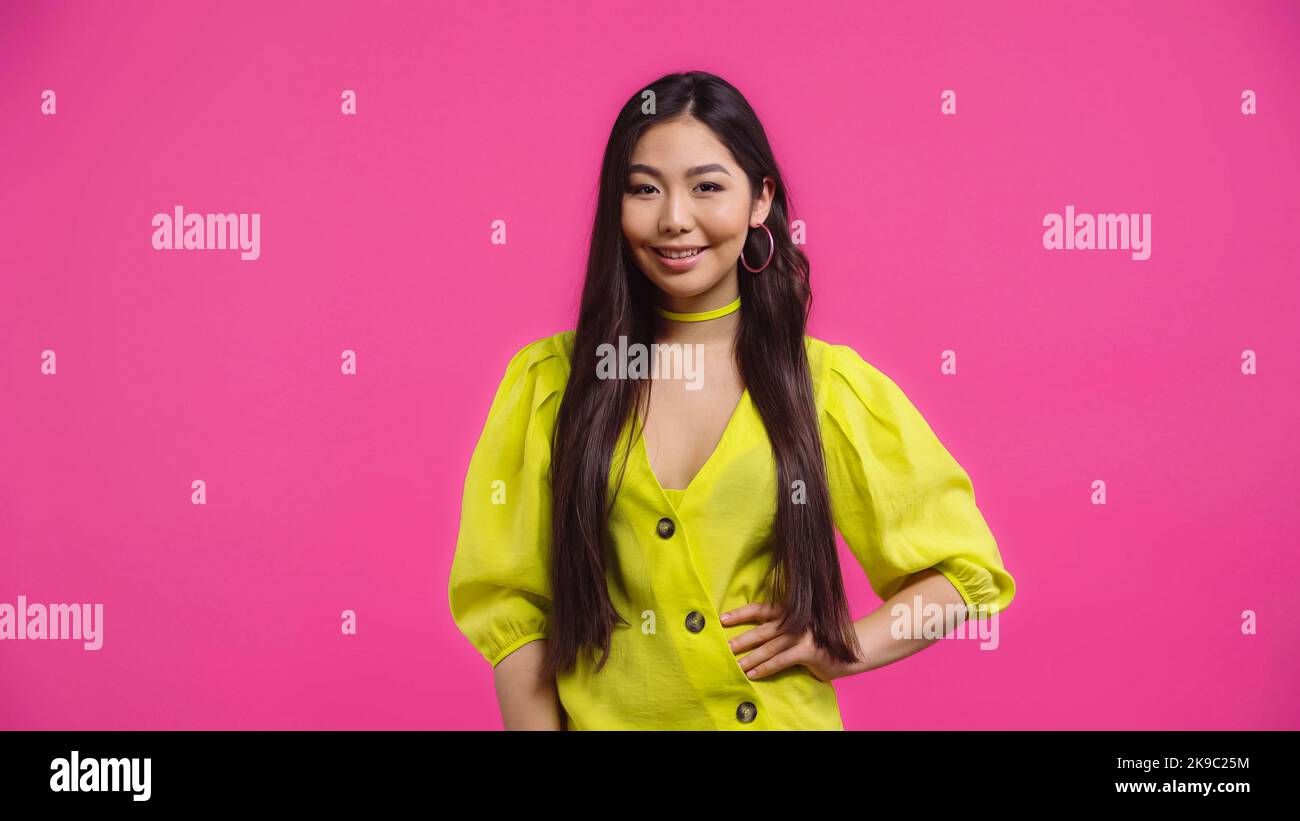 happy asian woman standing with hand on hip isolated on pink Stock ...