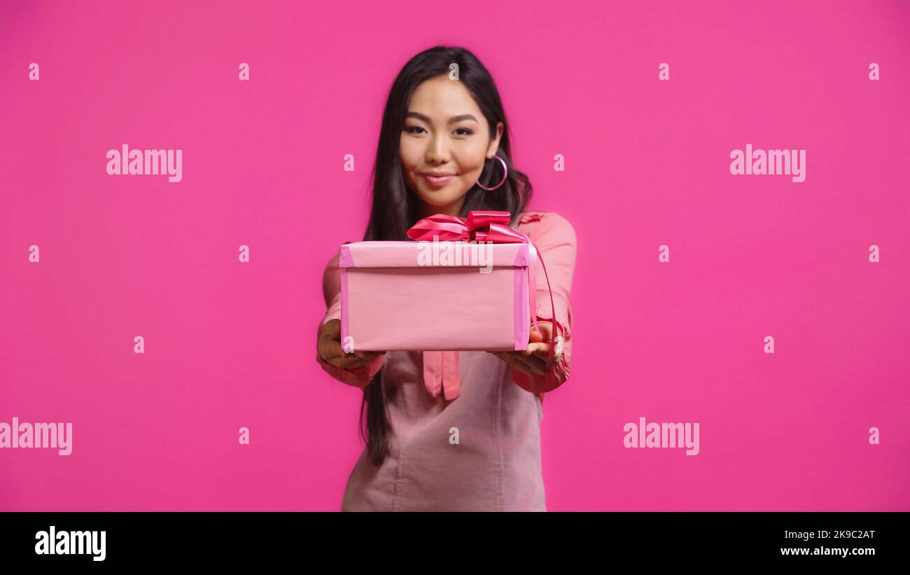 pleased young asian woman holding wrapped present isolated on pink Stock Photo