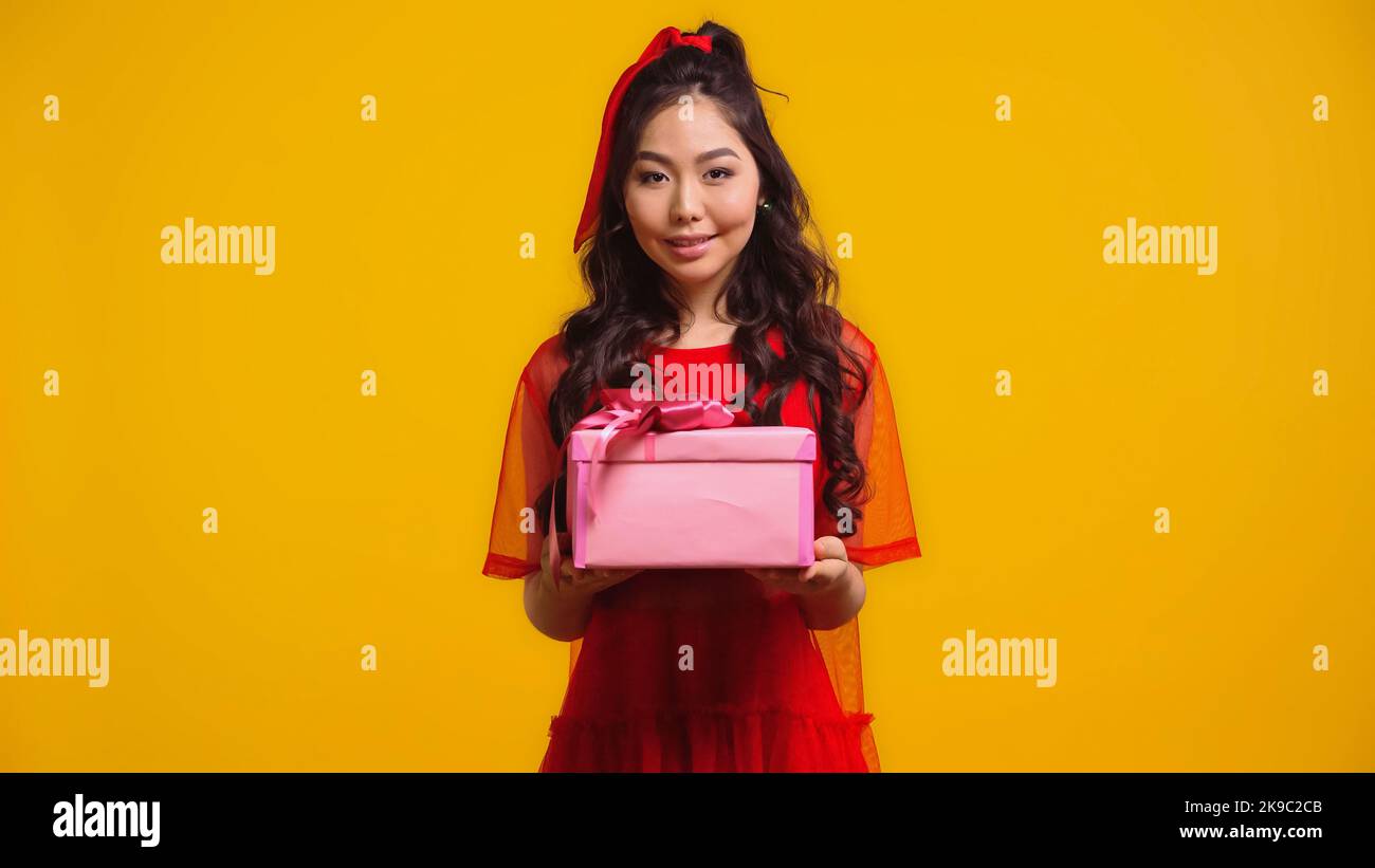 cheerful and young asian woman holding wrapped present isolated on yellow Stock Photo