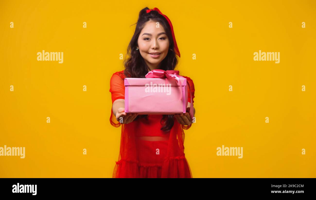 smiling young asian woman holding wrapped present isolated on yellow Stock Photo
