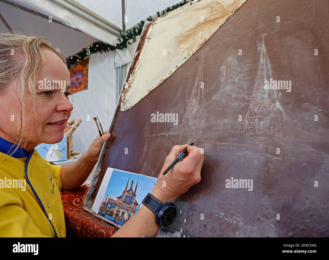 Wernigerode, Germany. 27th Oct, 2022. Master confectioner Dörte Schetter from Metzingen engraves the image of Wernigerode's town hall on a chocolate bar. Until 31.10. numerous suppliers of chocolate products present their goods on the market square and Nikolaiplatz. Germany's largest chocolate festival celebrates its 10th anniversary this year. Top chocolatiers from different countries are guests in Wernigerode this year. Credit: Matthias Bein/dpa/ZB/dpa/Alamy Live News Stock Photo