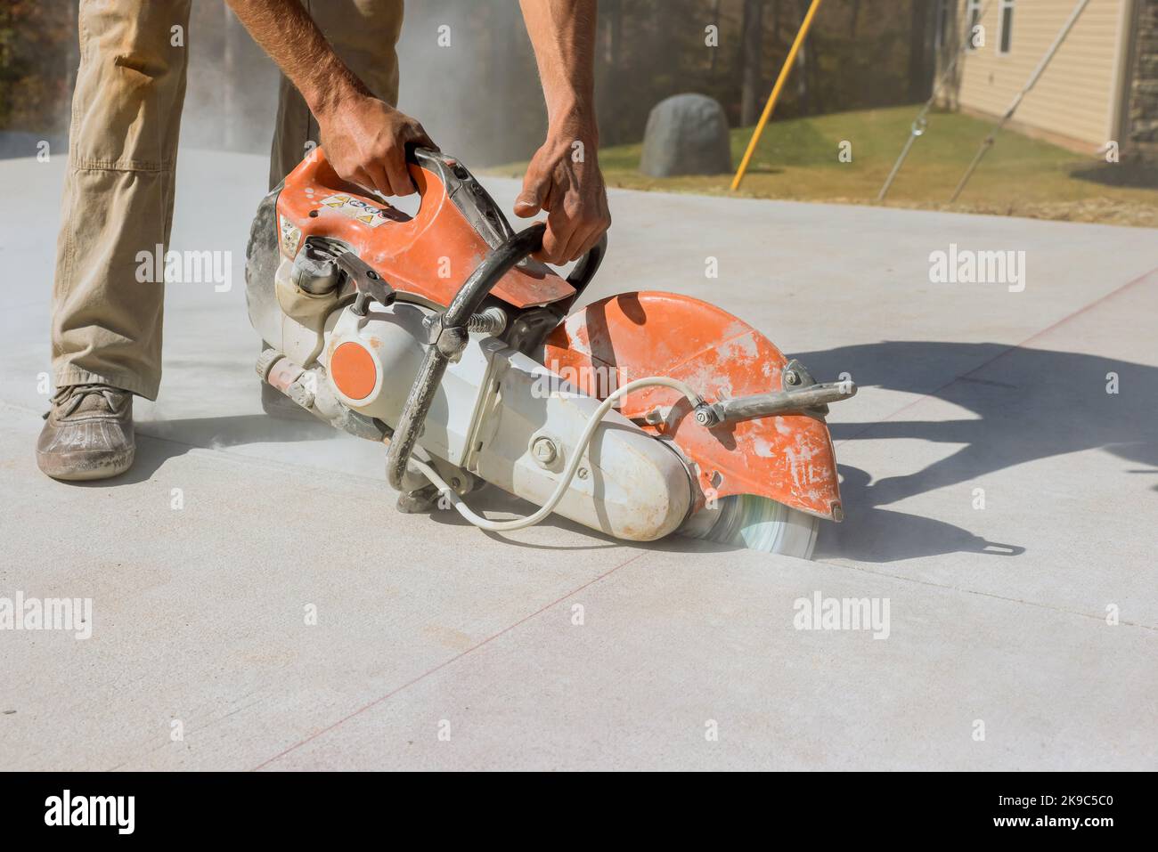Using diamond bladed saw machine, construction worker cuts concrete sidewalks Stock Photo