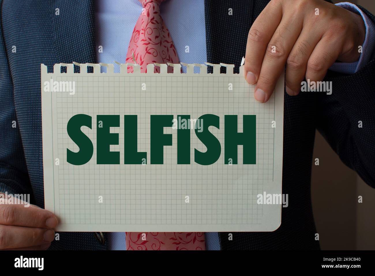 The paper in the hand of the man in the suit reads ''selfish''. Stock Photo