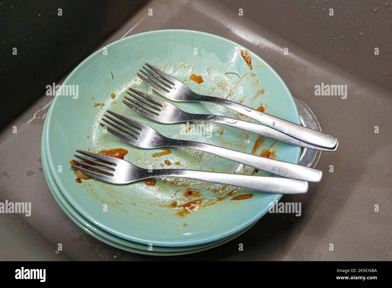 Dirty plates with four forks in a kitchen sink, top view Stock Photo