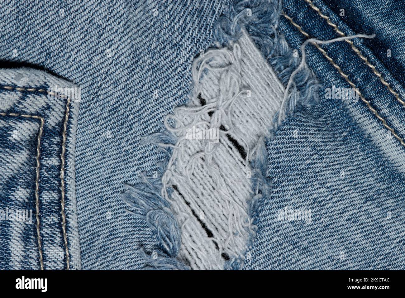 Torn blue denim clothing with pocket seams and stitching. Flat lay worn out jeans isolated section. Stock Photo