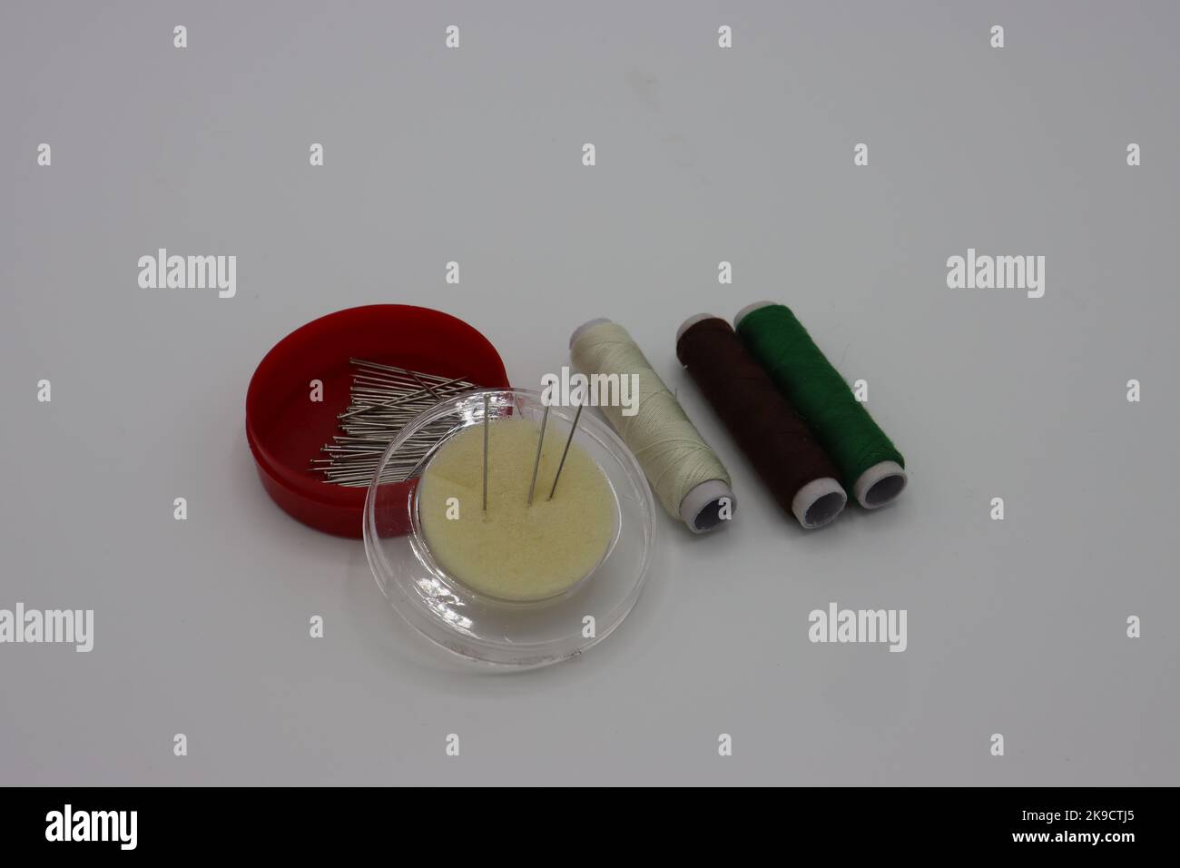Sewing accessories on a white background. Pins in a circular plastic box, threads Stock Photo