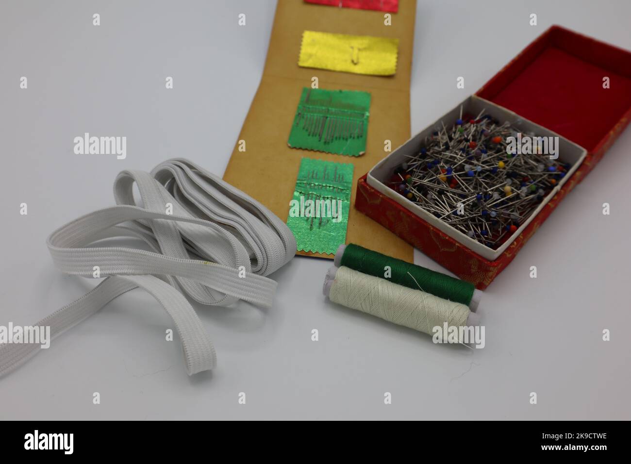 Sewing accessories on a white background. Needles in a paper holder, rubber band, pins in a box