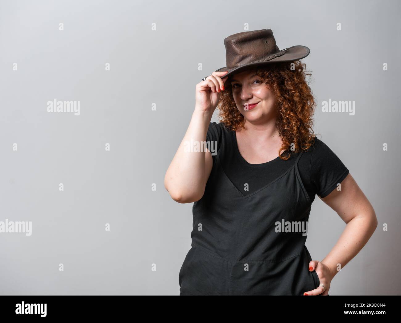 Happy woman with red curly hair posing on grey background, with copy