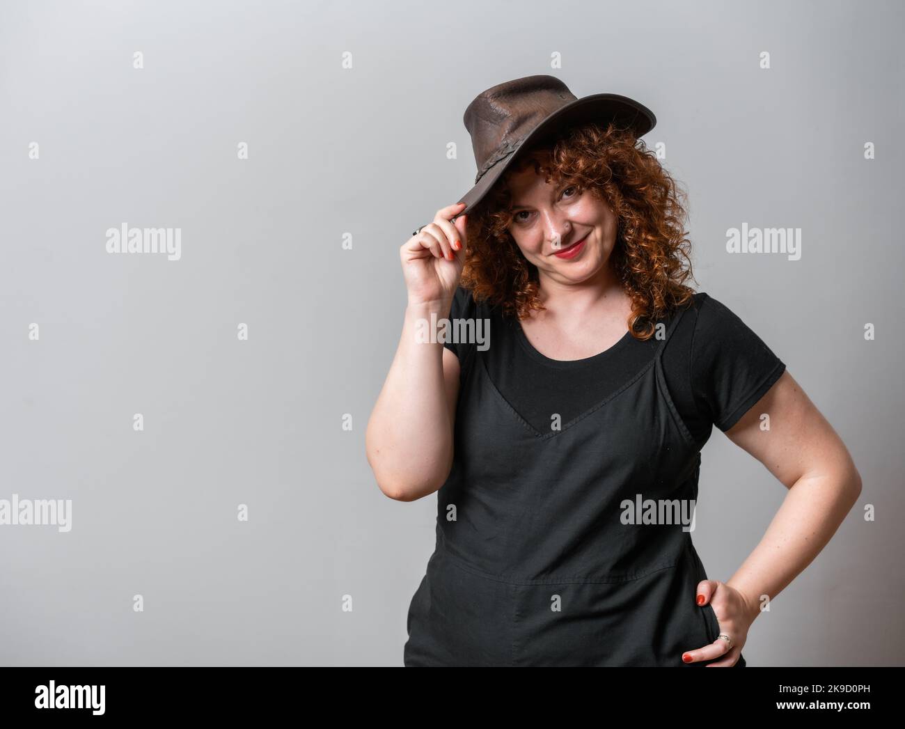 Happy woman with red curly hair posing on grey background, with copy