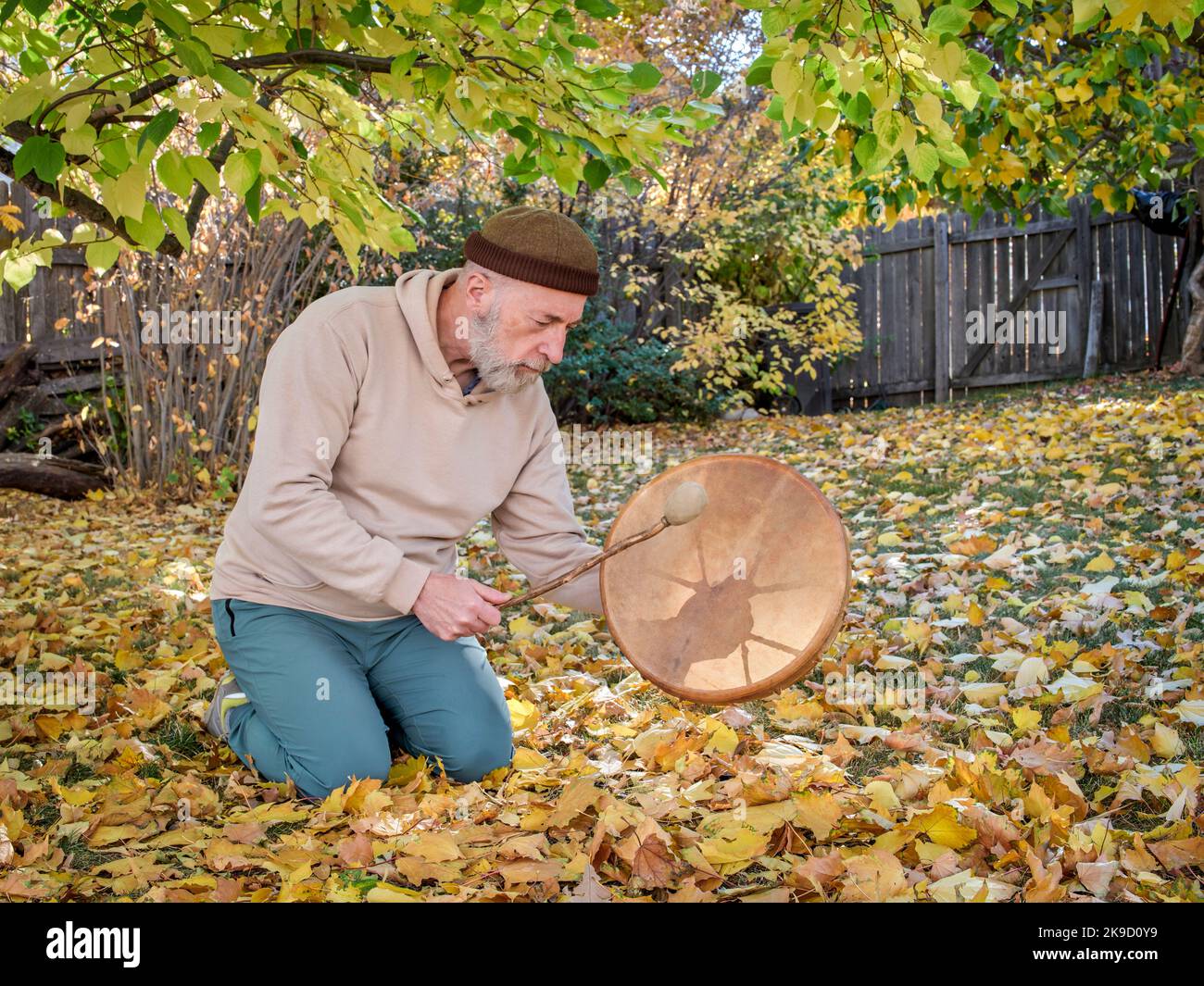 senior man is sitting in seiza position and  playing a shaman drum in a fall scenery Stock Photo
