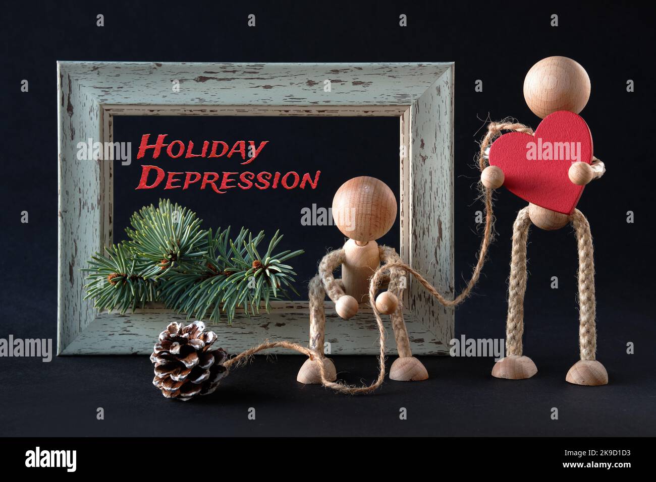 Holiday depression text. Mental disorder, despair. Wooden toy figurines, men by textured frame with fir twig and frosted pine cone. One man holds red Stock Photo