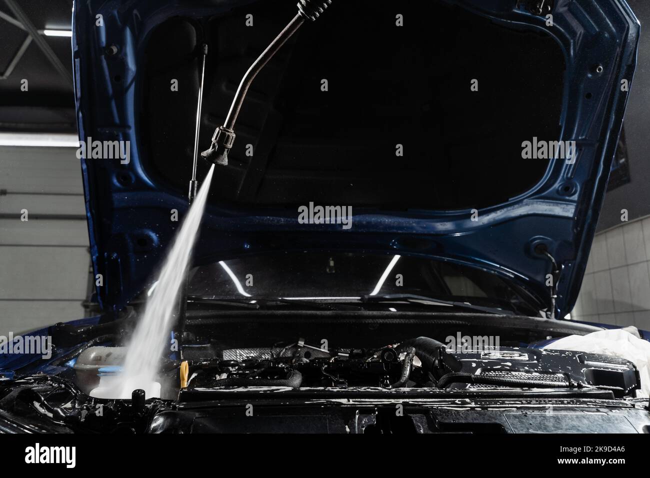 Pouring water on car engine. Washing car engine with spray, brush and