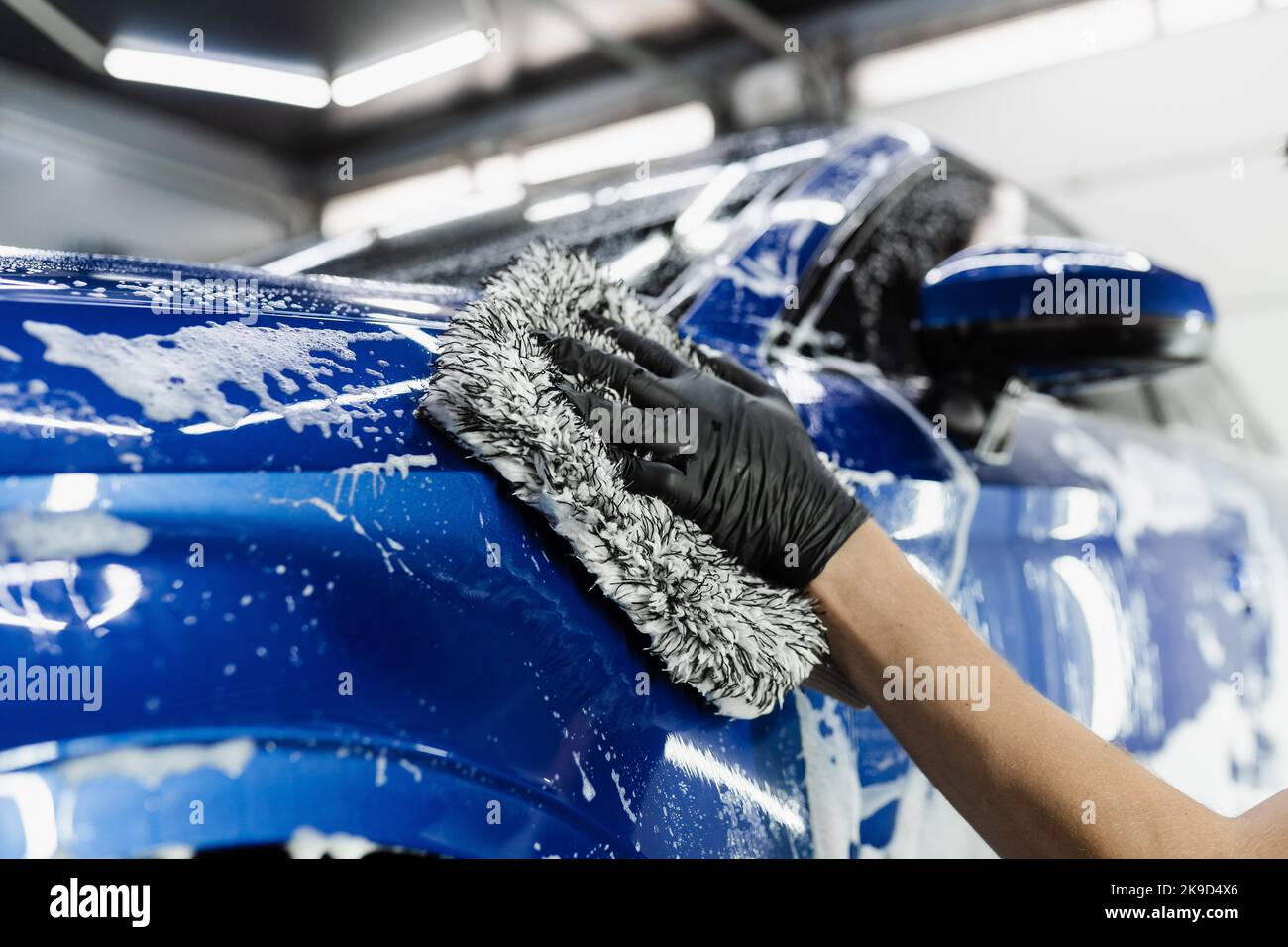 Hand washing with microfiber glove with foam car body in garage. Car