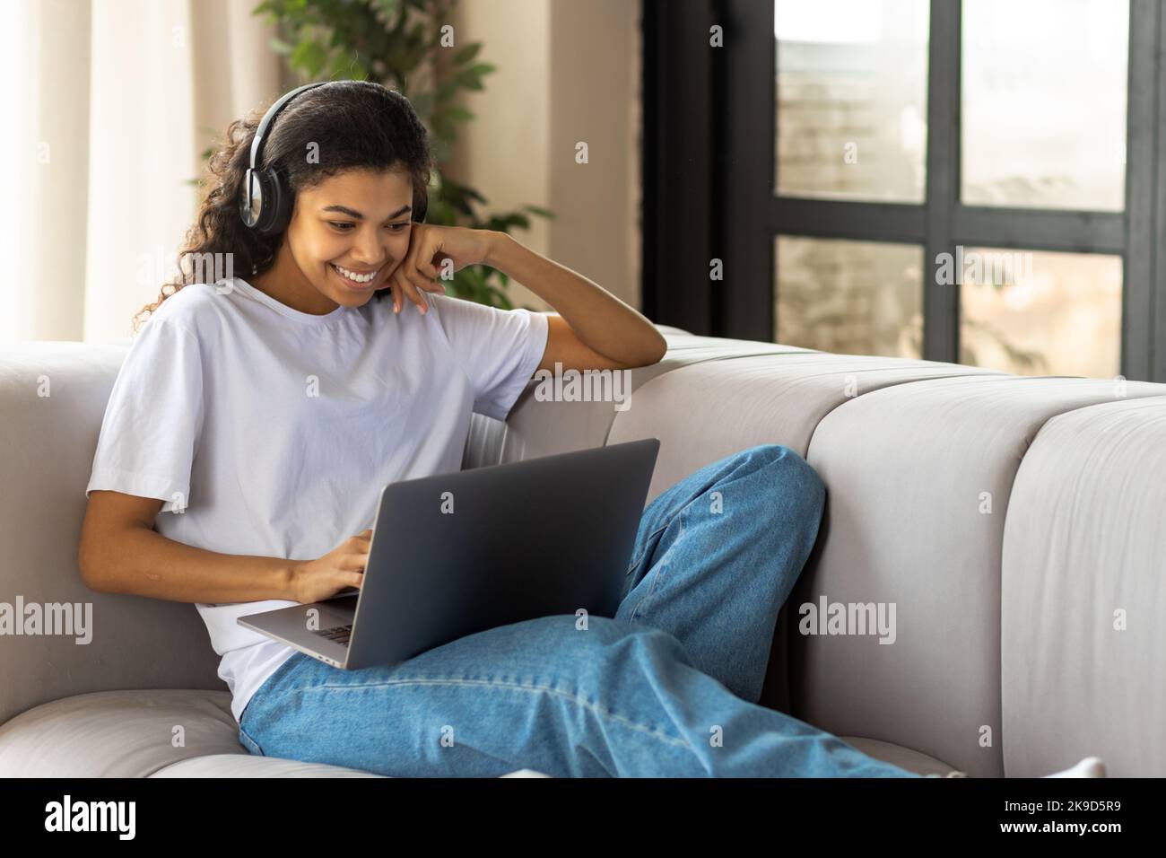 African American woman in earphone with Afro hair using a laptop talking to webcam with friend online Stock Photo