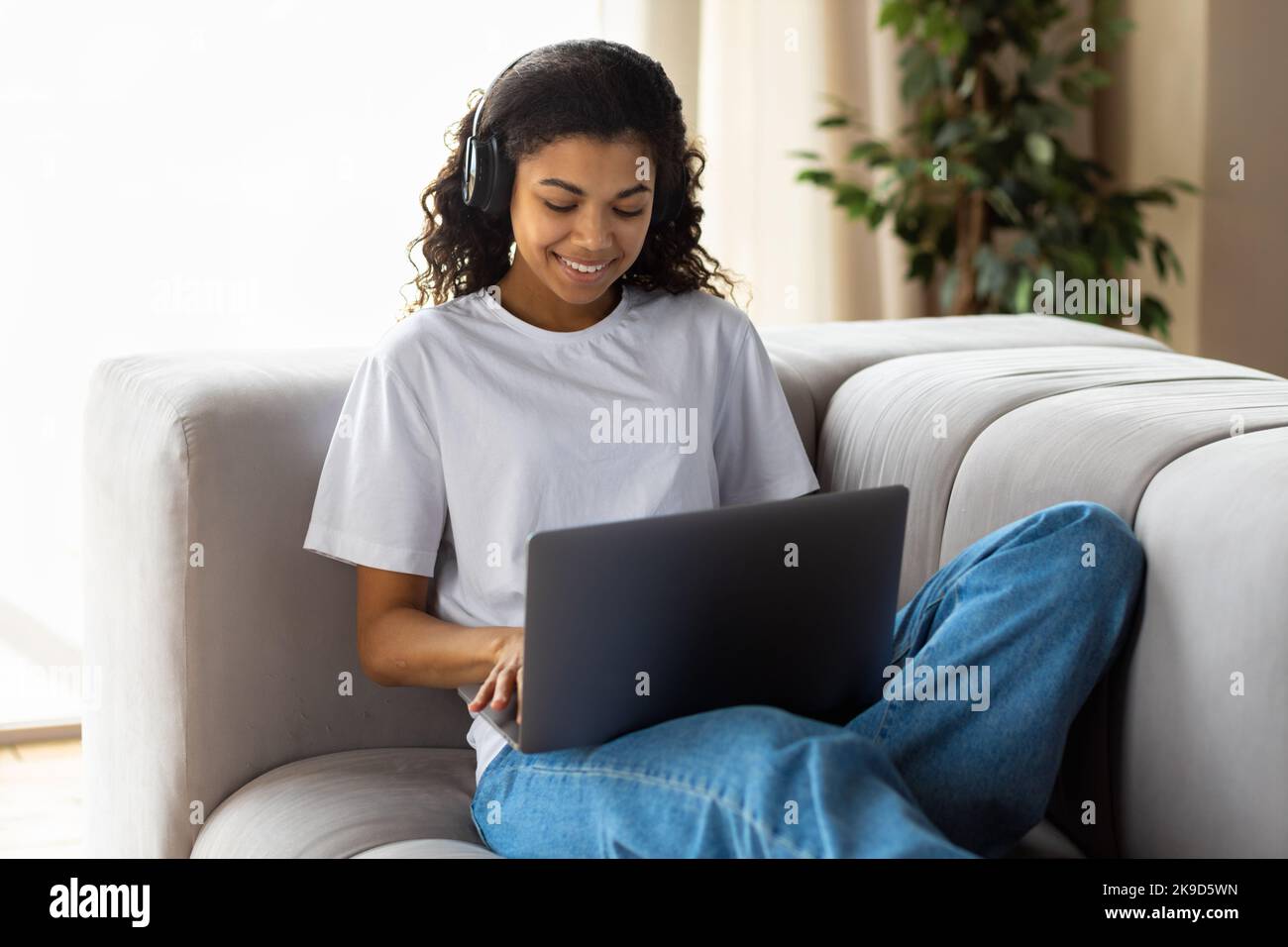 Young African American hipster woman in earphone using a laptop talking to webcam with friend online Video call Stock Photo