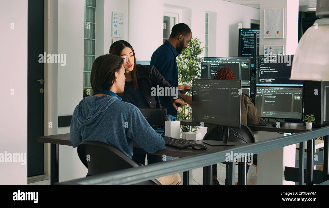 Asian team of artificial intelligence cloud programers talking about programming in it agency office. Compiling code on terminal window server, doing teamwork on developing algorithms. Stock Photo
