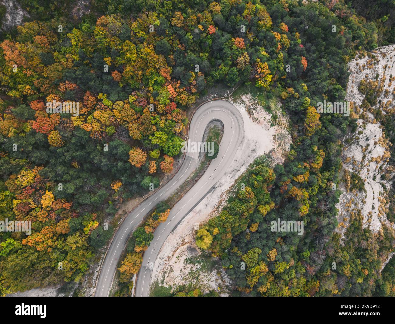 Aerial view of a winding road from a high mountain pass through a dense ...
