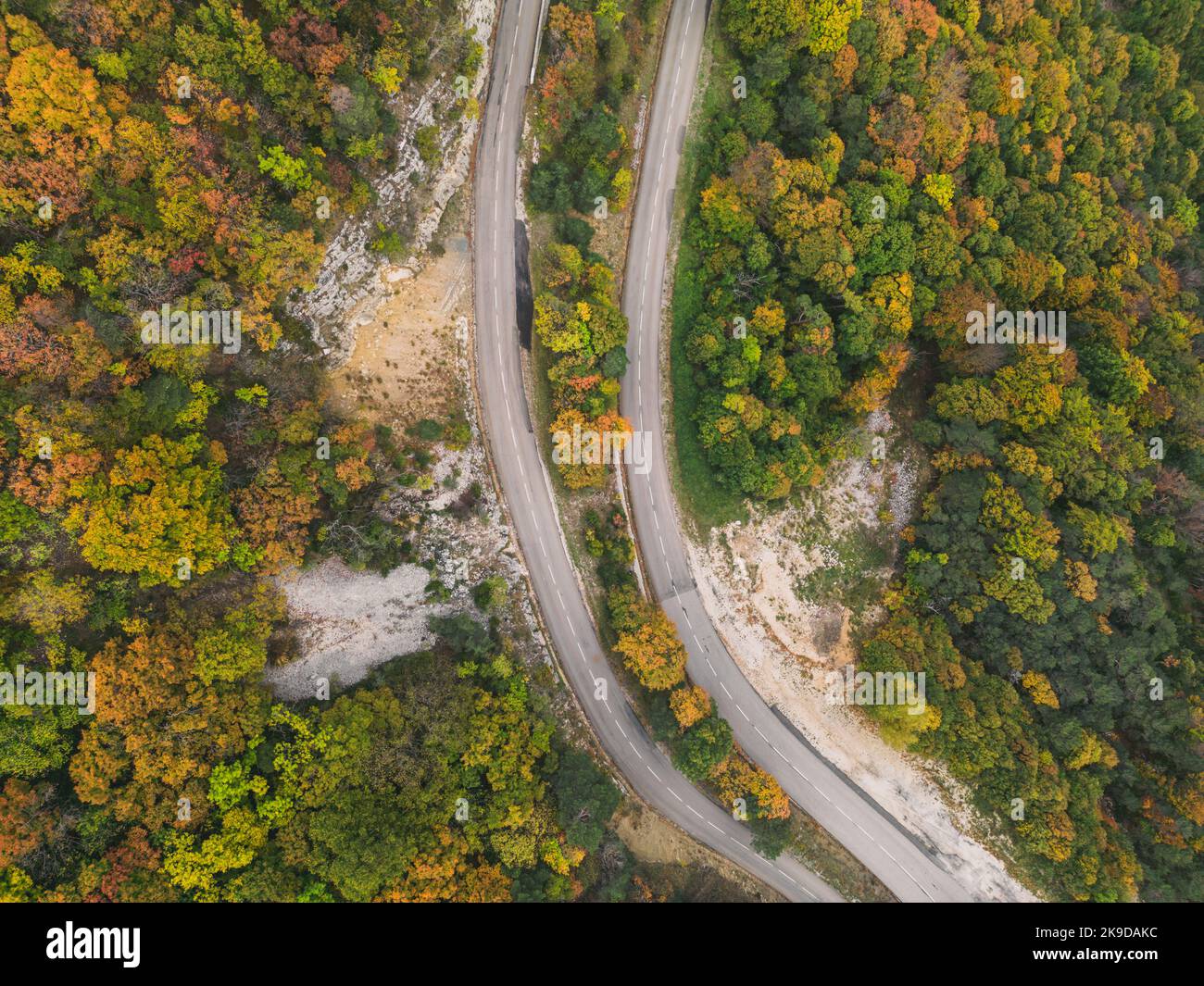 Aerial view of a winding road from a high mountain pass through a dense ...