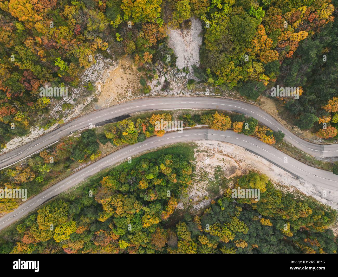 Aerial view of a winding road from a high mountain pass through a dense ...