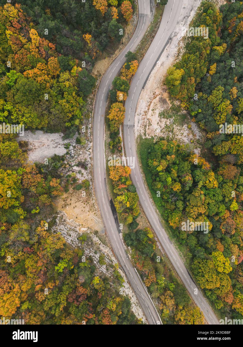 Aerial view of a winding road from a high mountain pass through a dense ...