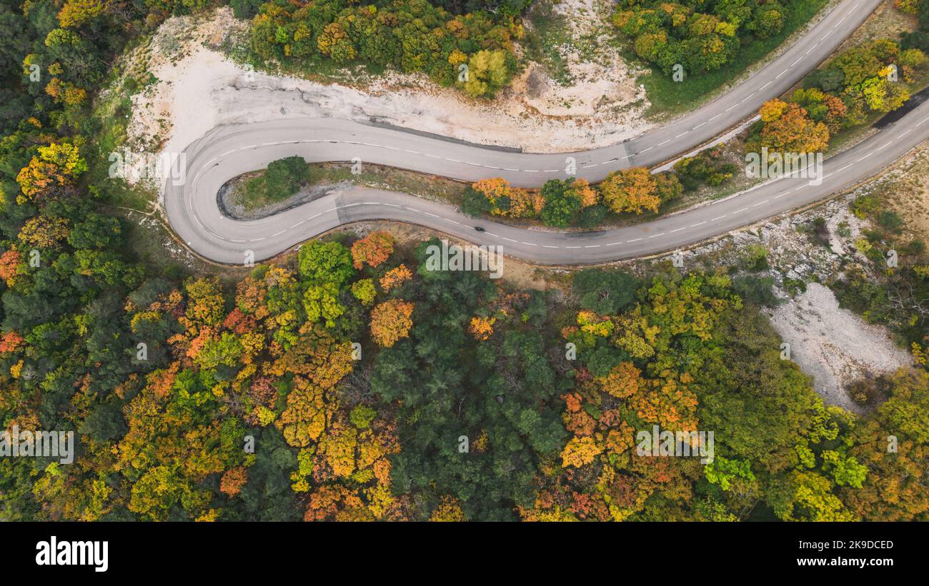 Aerial view of a winding road from a high mountain pass through a dense ...
