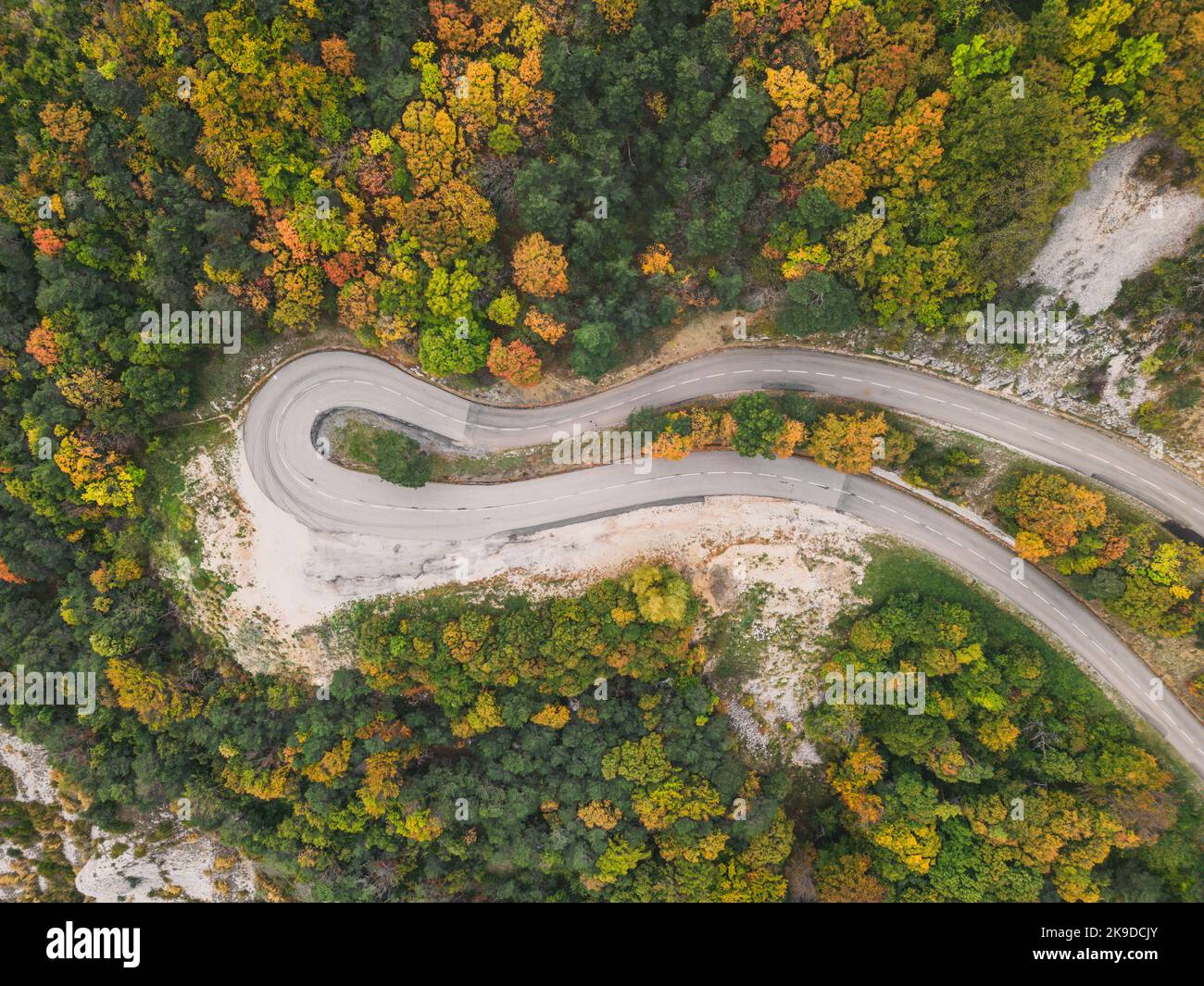 Aerial view of a winding road from a high mountain pass through a dense ...