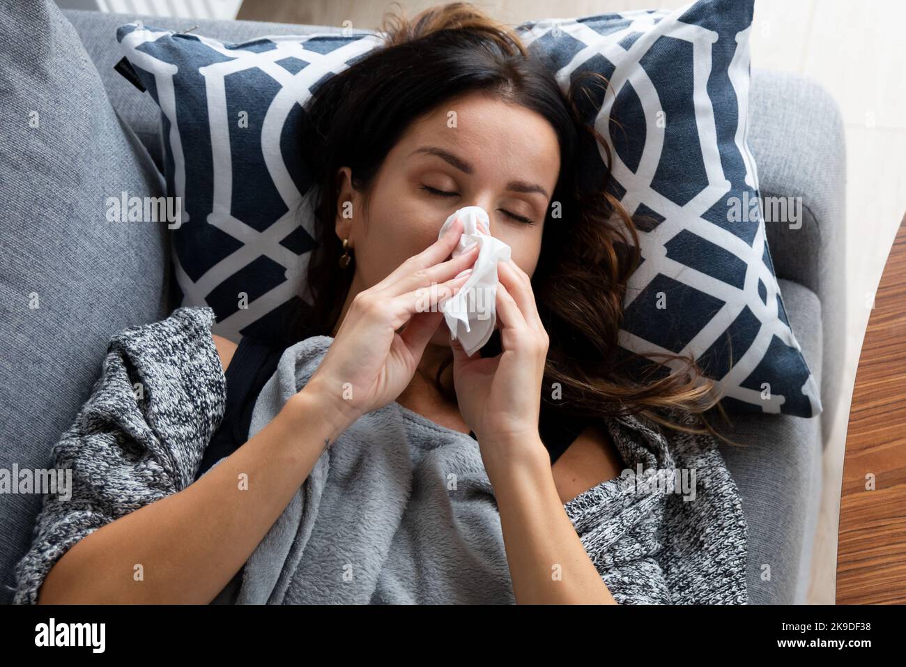 Sick woman blows her nose into a handkerchief, lying on bed Stock Photo