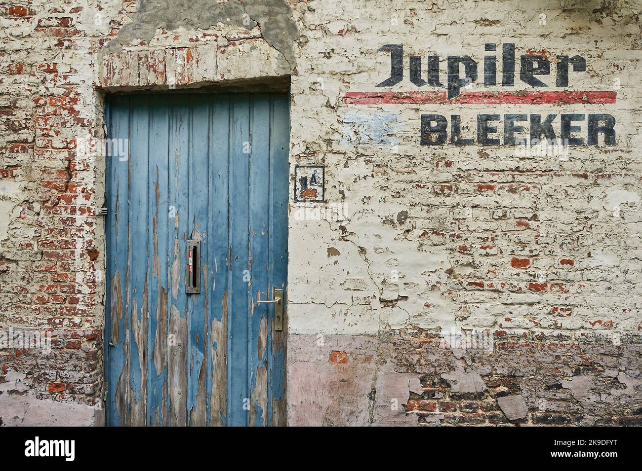 Old blue door in a white washed brick wall with Jupiler Bleeker stencilled alongside Stock Photo