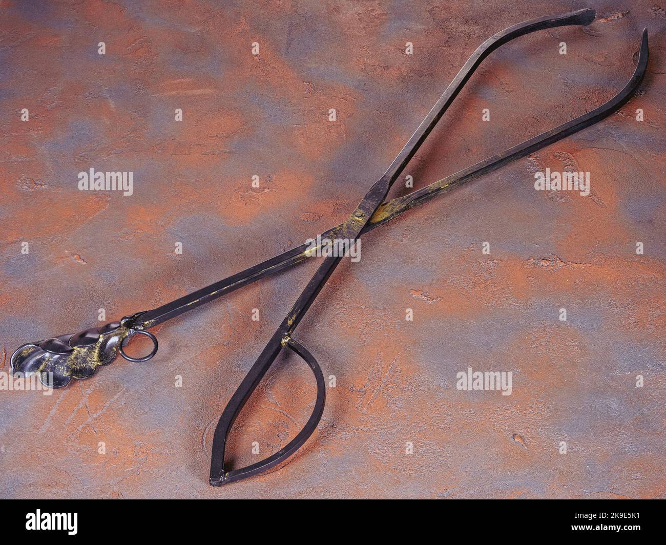 Metal tongs for coals as fireplace accessories on a grunge rusty background Stock Photo