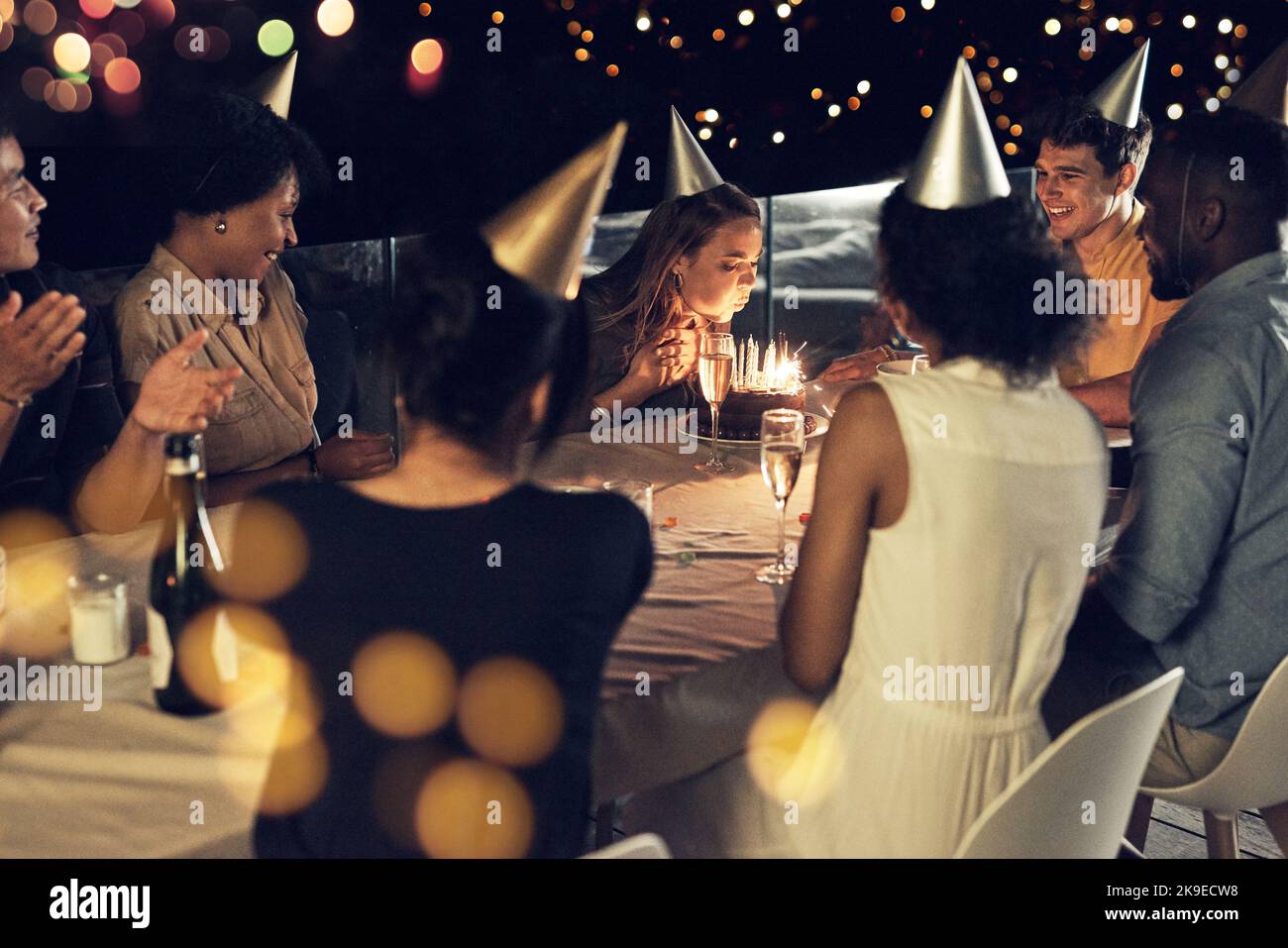 The birthday girl doing her thing. a beautiful young woman blowing at the candles on her birthday cake at a evening gathering with friends. Stock Photo