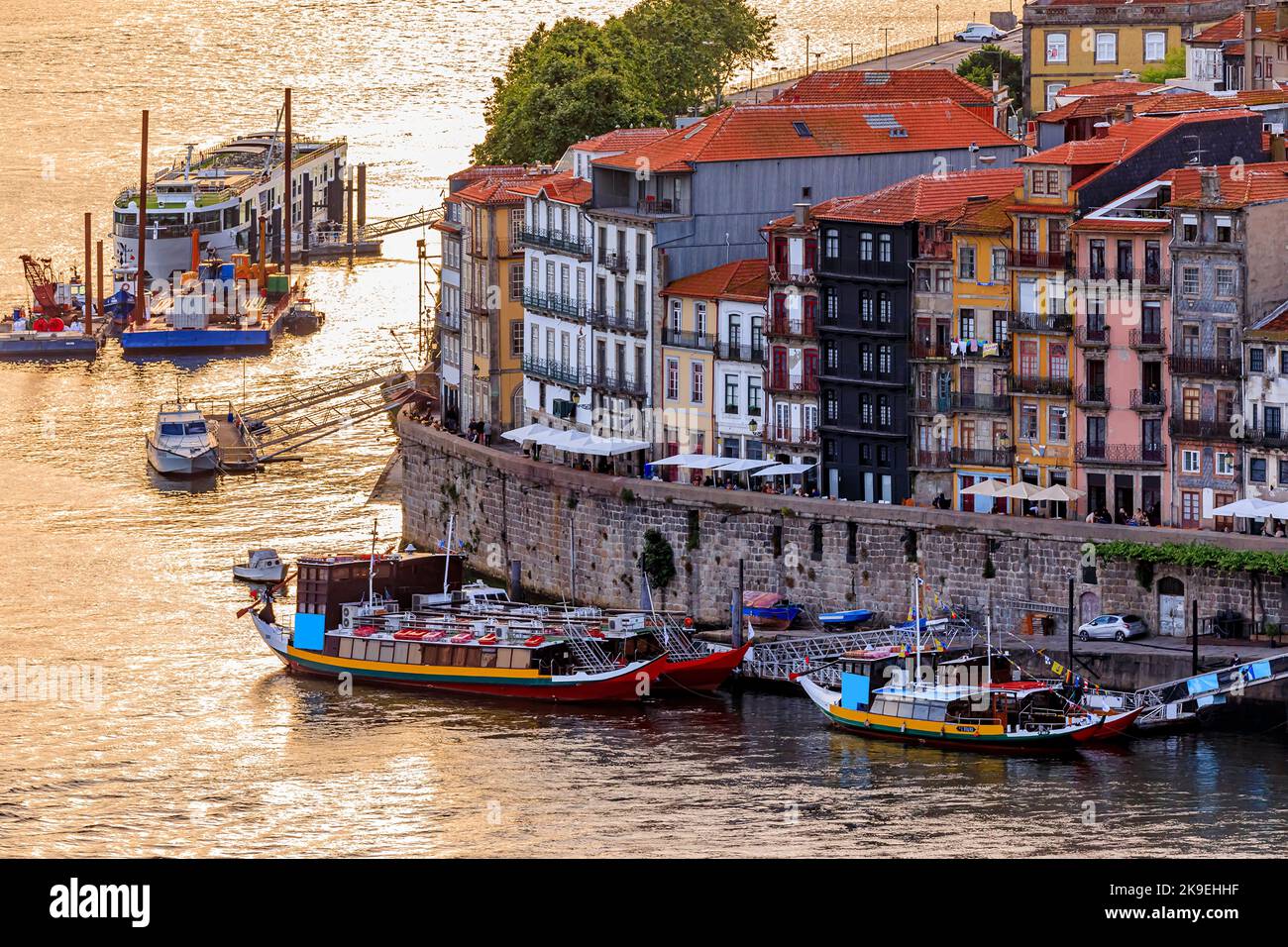 Facades of traditional colorful Portuguese houses in Ribeira and rabelo boats docked on Douro at sunset golden hour, Porto, Portugal Stock Photo