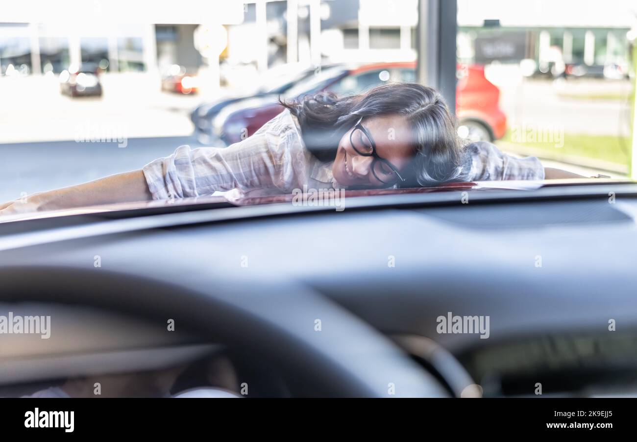 Excited woman hugging her new dream red car in a car dealership. Stock Photo