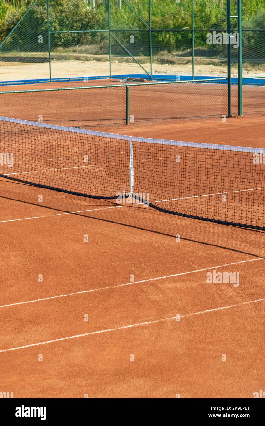 Baseline and net of an empty clay tennis court on a sunny day Stock Photo