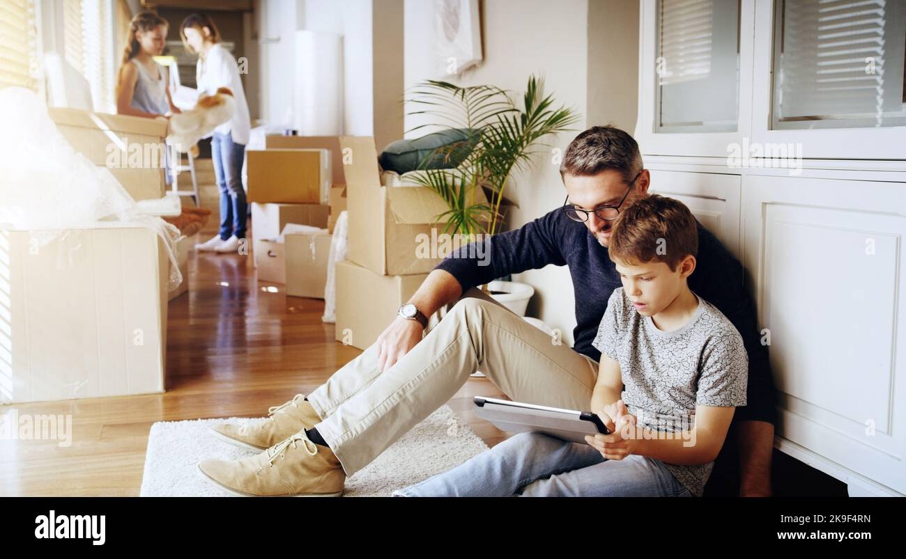 Trying to get the wifi all connected and working. a father and his son using a digital tablet while moving in to their new house with their family. Stock Photo