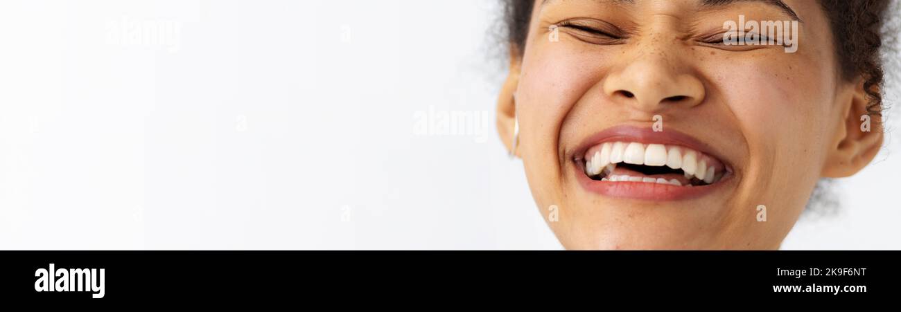Portrait young happy positive African American woman with white teeth smiling broadly keeps eyes closed Stock Photo
