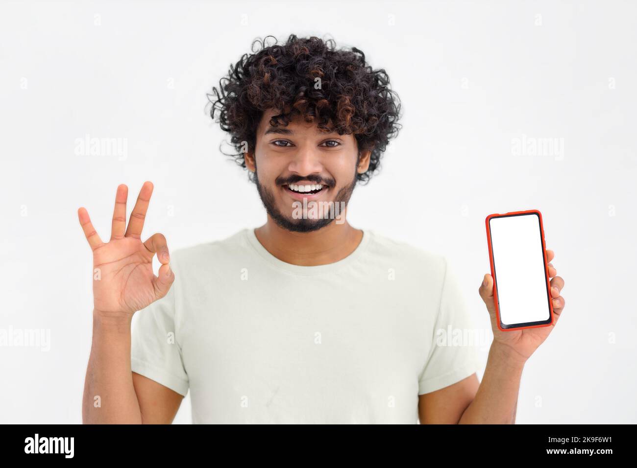 Portrait of young Asian man with mobile phone on white background. Male with curly hair holding a smartphone Stock Photo