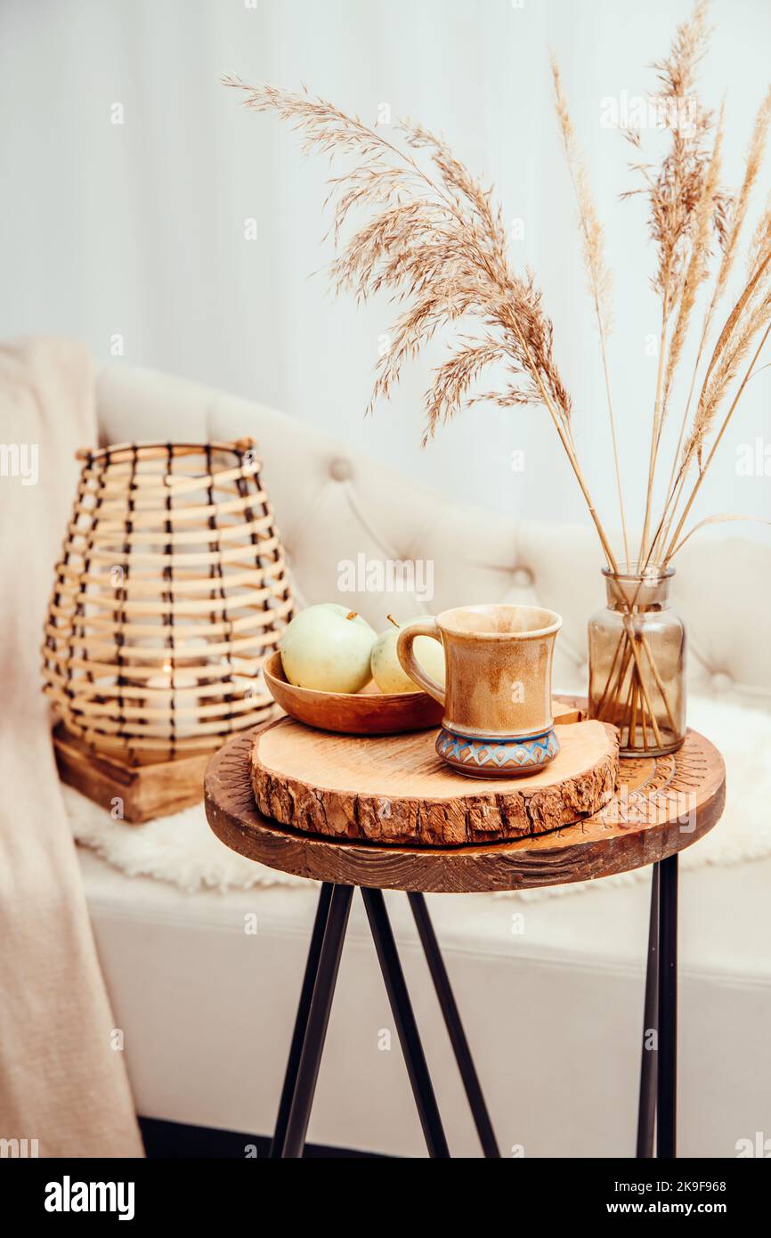 Cozycore or cottagecore concept, warm soft brown beige interior design objects. Cozy wool plaid on sofa, candle burning in wood lantern, tea cup. Stock Photo