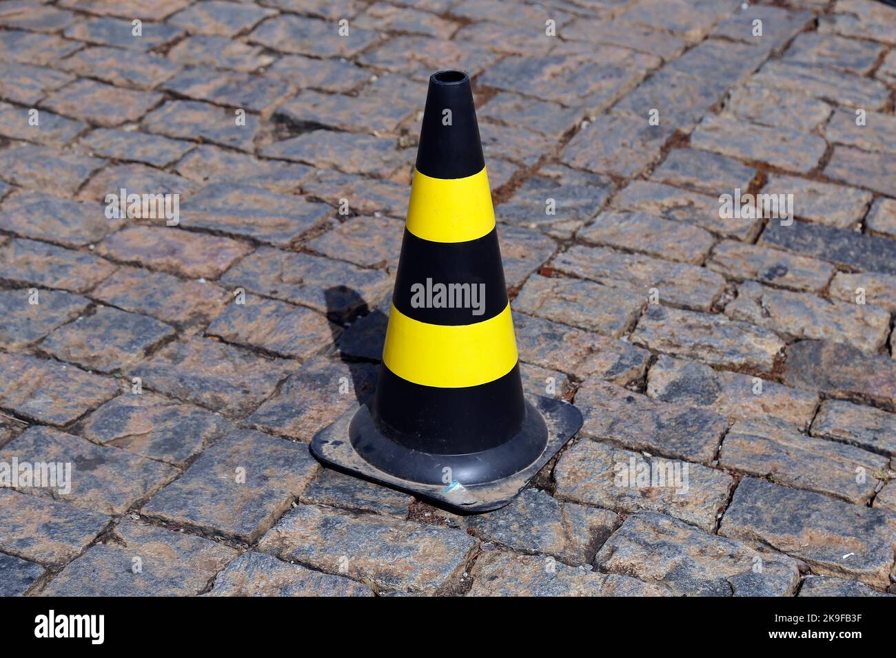 traffic signal cone yellow and black colors, hard plastic, on stone